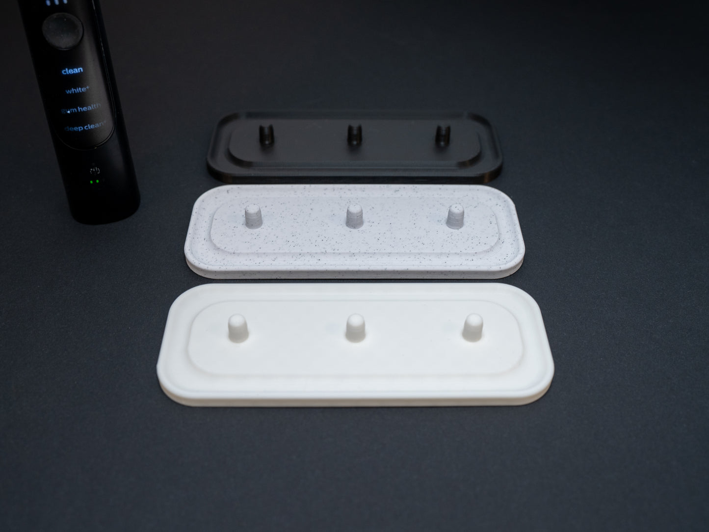 Philips Sonicare electric toothbrush stands that hold three toothbrushes shown in white, white stone effect and black.