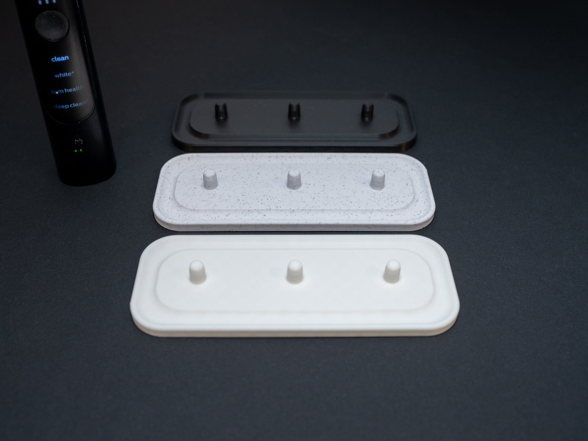 Philips Sonicare electric toothbrush stands that hold three toothbrushes shown in white, white stone effect and black.