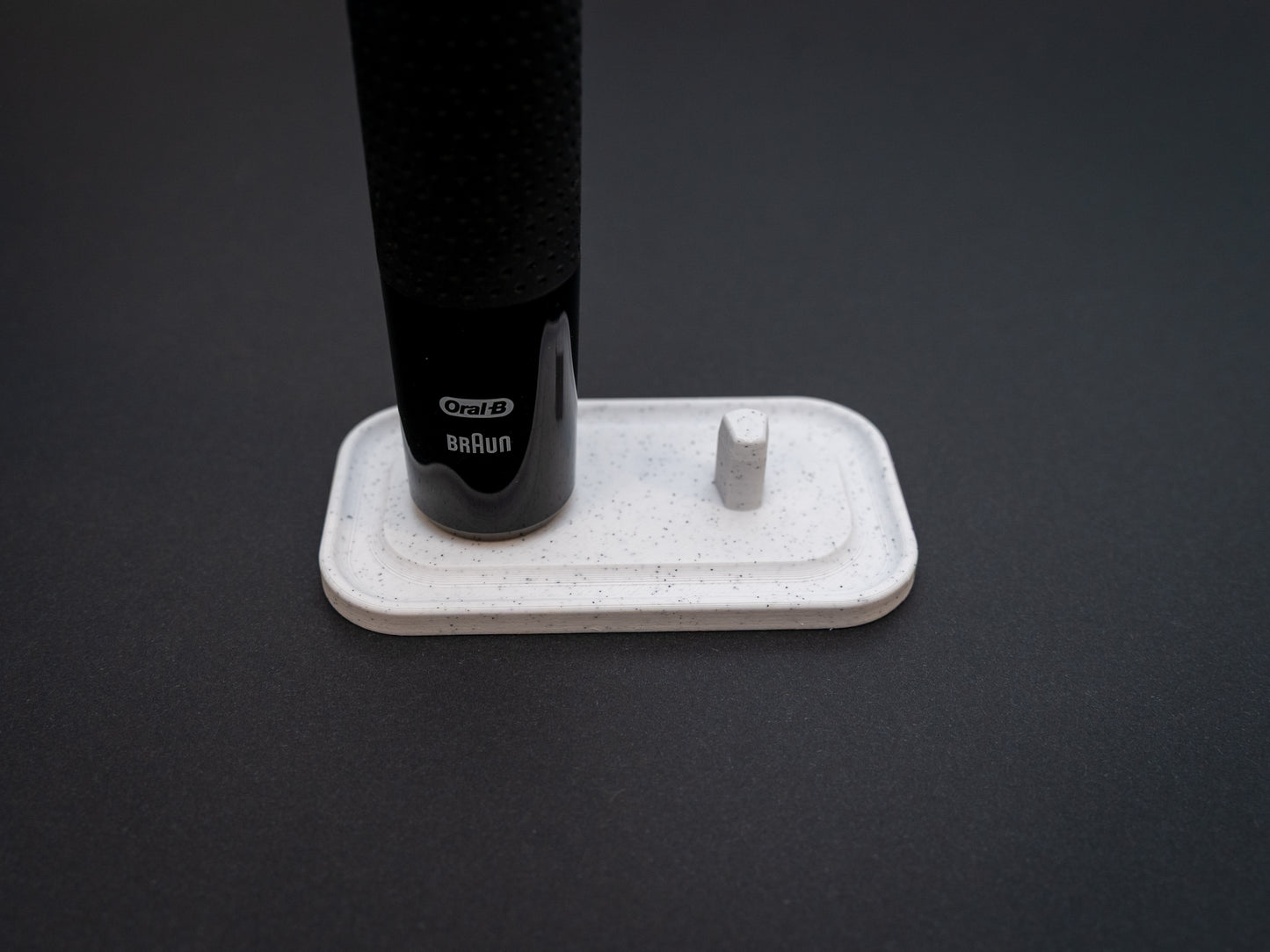 3D printed Oral B toothbrush stand in white marble stone colour on a black background. Picture shows a stand for two toothbrushes. Stops toothbrush from falling over and organises the bathroom