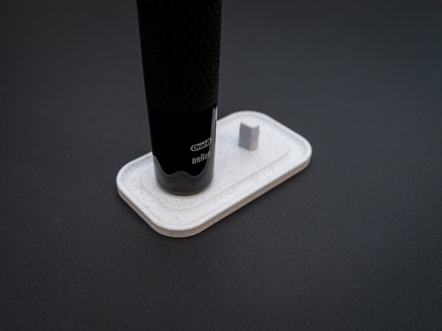 3D printed Oral B toothbrush stand in white marble stone colour on a black background. Picture shows a stand for two toothbrushes. Stops toothbrush from falling over and organises the bathroom
