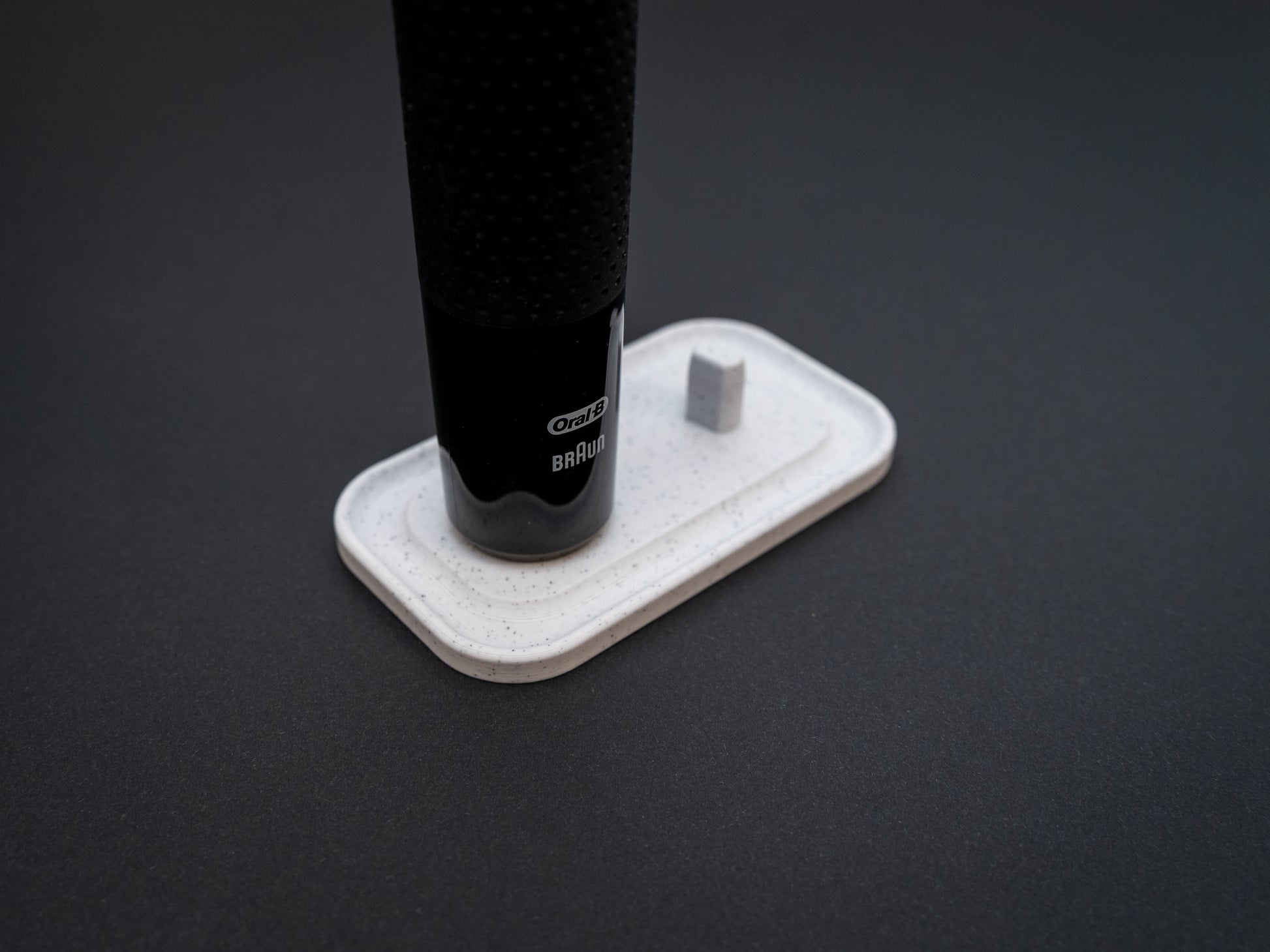 3D printed Oral B toothbrush stand in white marble stone colour on a black background. Picture shows a stand for two toothbrushes. Stops toothbrush from falling over and organises the bathroom