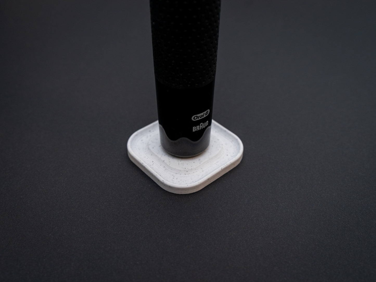 3D printed Oral B toothbrush stand in white marble stone colour on a black background. Picture shows a stand for one toothbrush. Stops toothbrush from falling over and organises the bathroom