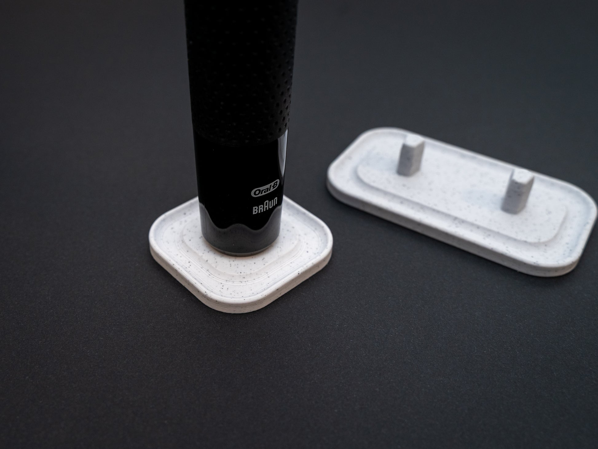3D printed Oral B toothbrush stand in white marble stone colour on a black background. Picture shows a stand for one toothbrush and one for two toothbrushes. Stops toothbrush from falling over and organises the bathroom