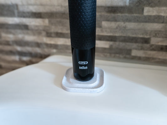 3D printed Oral B toothbrush stand in white marble stone colour on a bathroom sink. Stops toothbrush from falling over and organises the bathroom