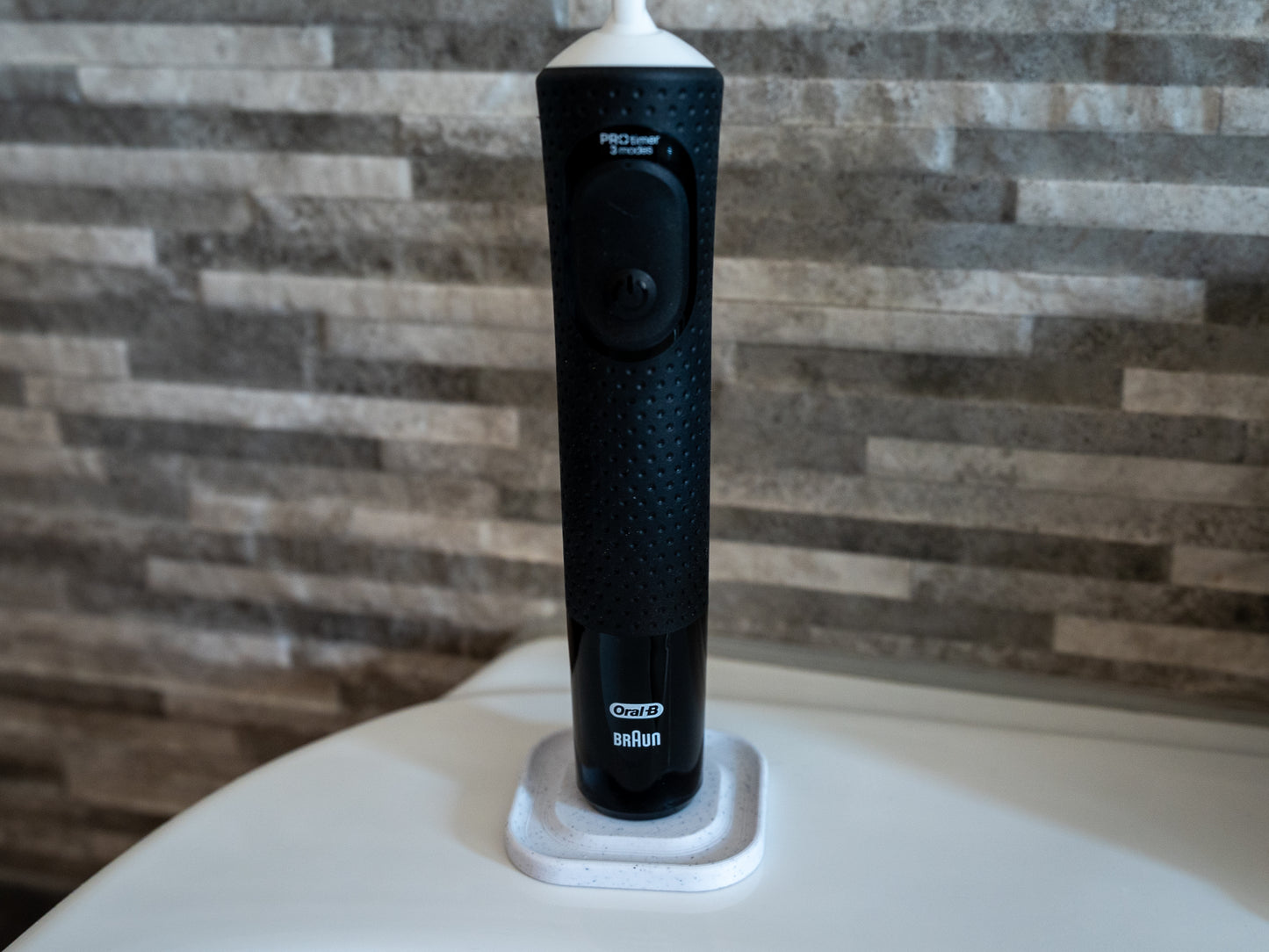 3D printed Oral B toothbrush stand in white marble stone colour on a bathroom sink. Stops toothbrush from falling over and organises the bathroom