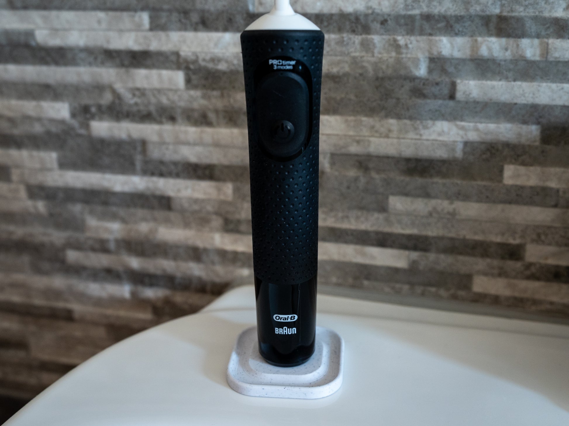3D printed Oral B toothbrush stand in white marble stone colour on a bathroom sink. Stops toothbrush from falling over and organises the bathroom